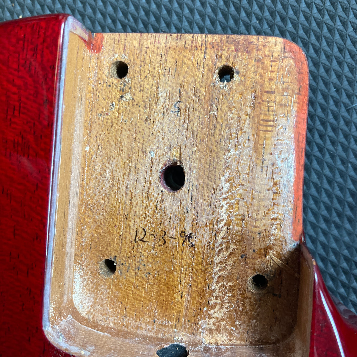 Close-up of the drilled neck pocket on an ESP Standard Eclipse Transparent Cherry Red w/Case by Esp; "12-3-96" handwritten on the surface, with the red guitar body and textured black background visible.