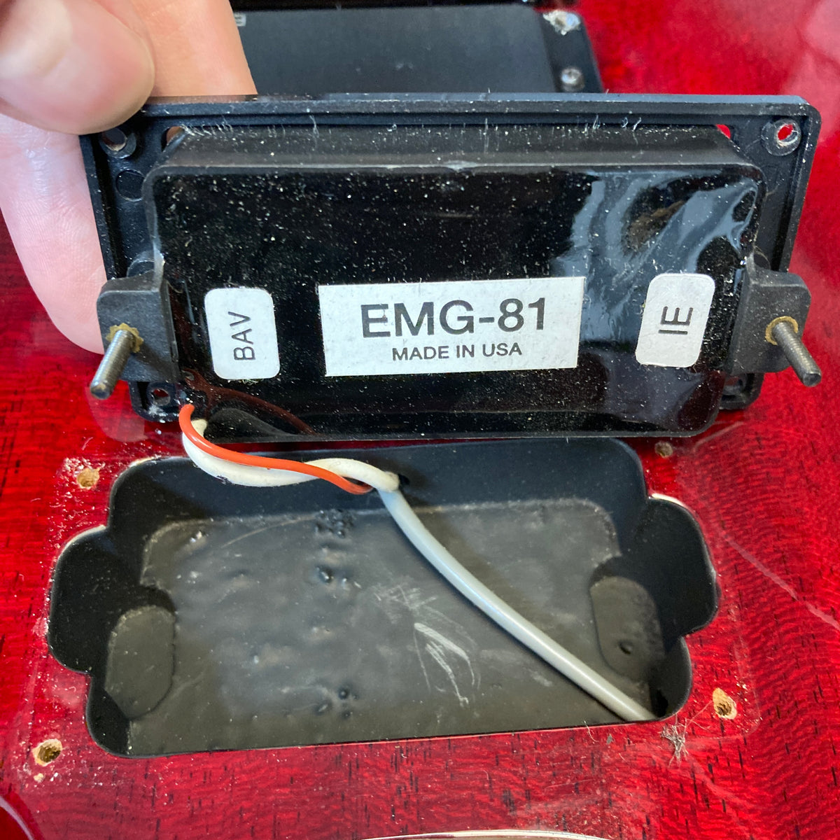Close-up of a hand lifting an EMG-81 pickup labeled "Made in USA," showing internal wiring and the pickup cavity of an ESP Standard Eclipse Transparent Cherry Red w/Case guitar by ESP.