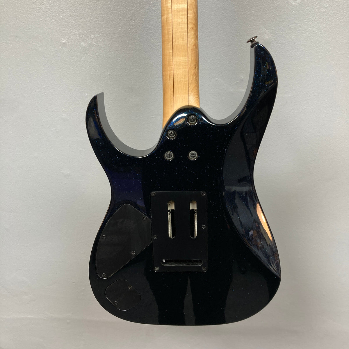 The back of the Ibanez Prestige RG1570 Cosmic Blue electric guitar features a sleek body, Wizard Prestige neck, exposed wood, and visible compartments for electronics and hardware; includes case.