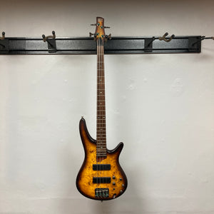 An Ibanez SDGR SR500PB four-string electric bass guitar by Ibanez, featuring a sunburst finish and flatwound strings, hangs on a wall rack against a plain white background. Includes hard case.