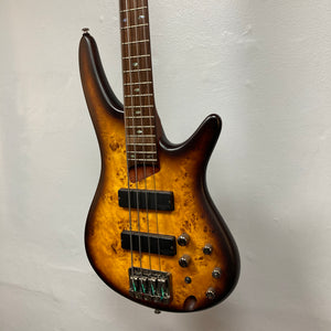 An Ibanez SDGR SR500PB five-string bass guitar by Ibanez, complete with hard case, hangs against a plain white wall.