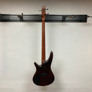 An Ibanez SDGR SR500PB bass guitar with hard case hangs on a wall-mounted rack, showing its back against a white wall.
