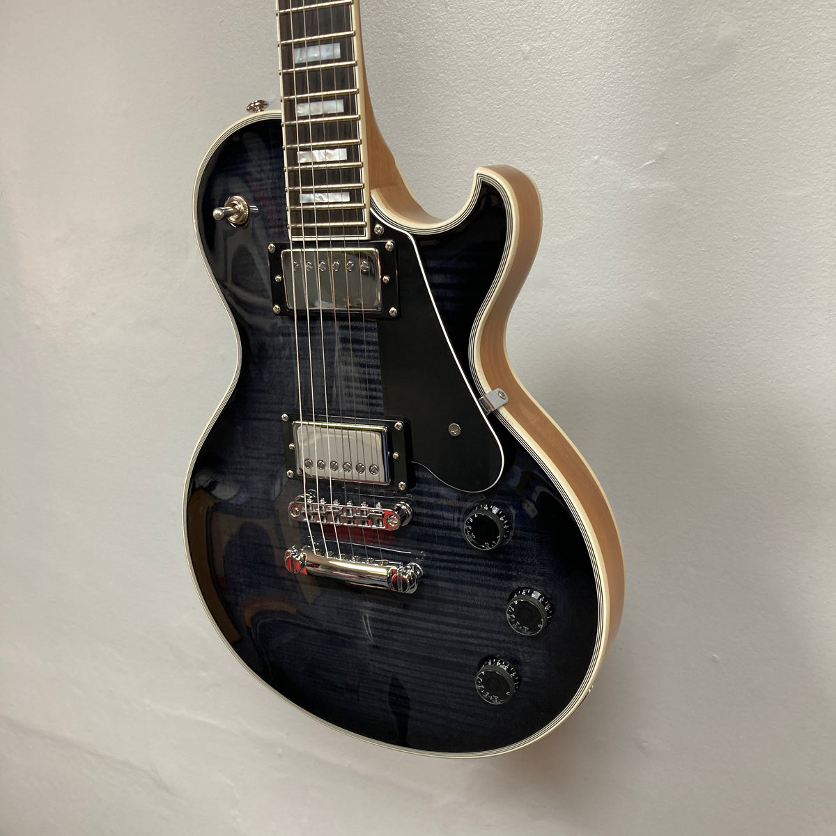 A used Schecter Solo-II Custom Trans Black Burst w/Case by Schecter hangs on a white wall, featuring chrome hardware, cream binding, black pickguard, and Pasadena USA pickups.