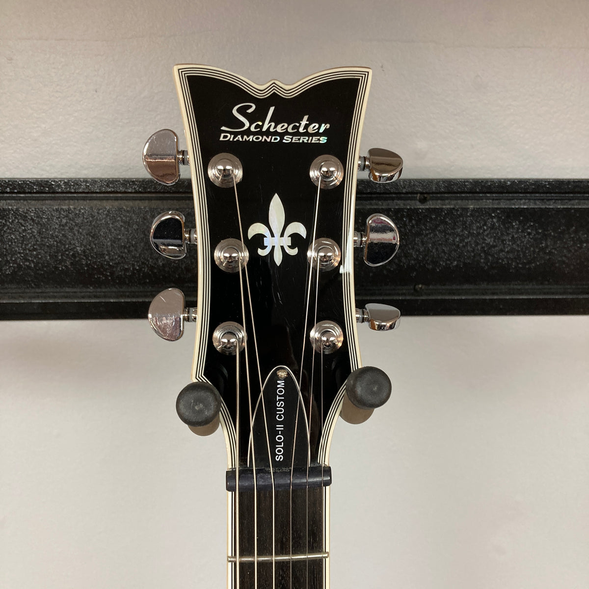 Close-up of a Schecter Solo-II Custom Trans Black Burst headstock with tuning pegs and fleur-de-lis inlay—featuring premium Schecter USA Pasadena pickups.
