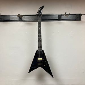 A black, USA-made 1992 Carvin Ultra V with a V-shaped body, Kahler Steeler tremolo, and MJ-wound Seymour Duncan DCJ humbucker hangs on a wall-mounted rack against a white wall.
