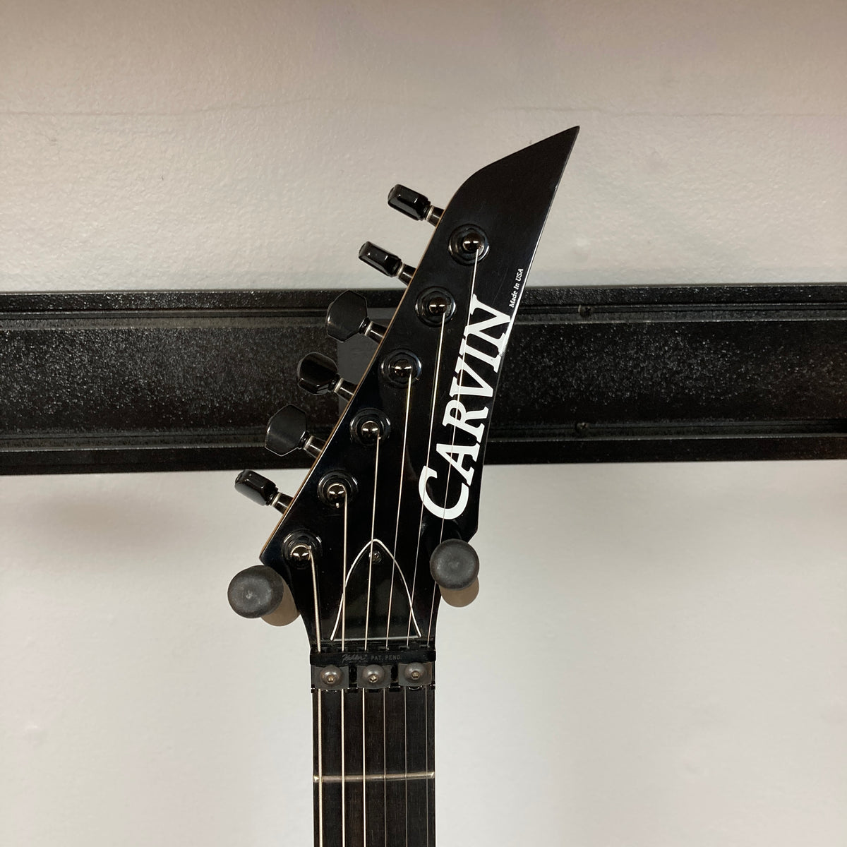 Headstock of a Carvin 1992 Ultra V USA with six tuners, black hardware, Kahler Steeler Trem, MJ‑wound Seymour Duncan DCJ pickup, and logo, shown against a white wall with a black horizontal bar.