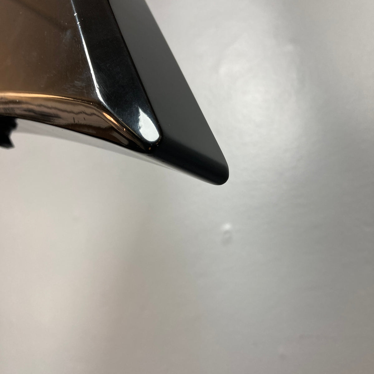 Close-up of the shiny black tip of a metallic object, likely from a Carvin 1992 Ultra V USA with Kahler Steeler Trem and MJ-wound Seymour Duncan DCJ, set against a plain light gray background.