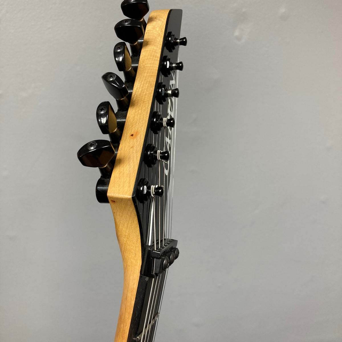 Close-up of a 1992 Carvin Ultra V USA headstock with six tuners and metal strings, featuring a Kahler Steeler Trem and MJ-wound Seymour Duncan DCJ, set against a plain light-colored wall.