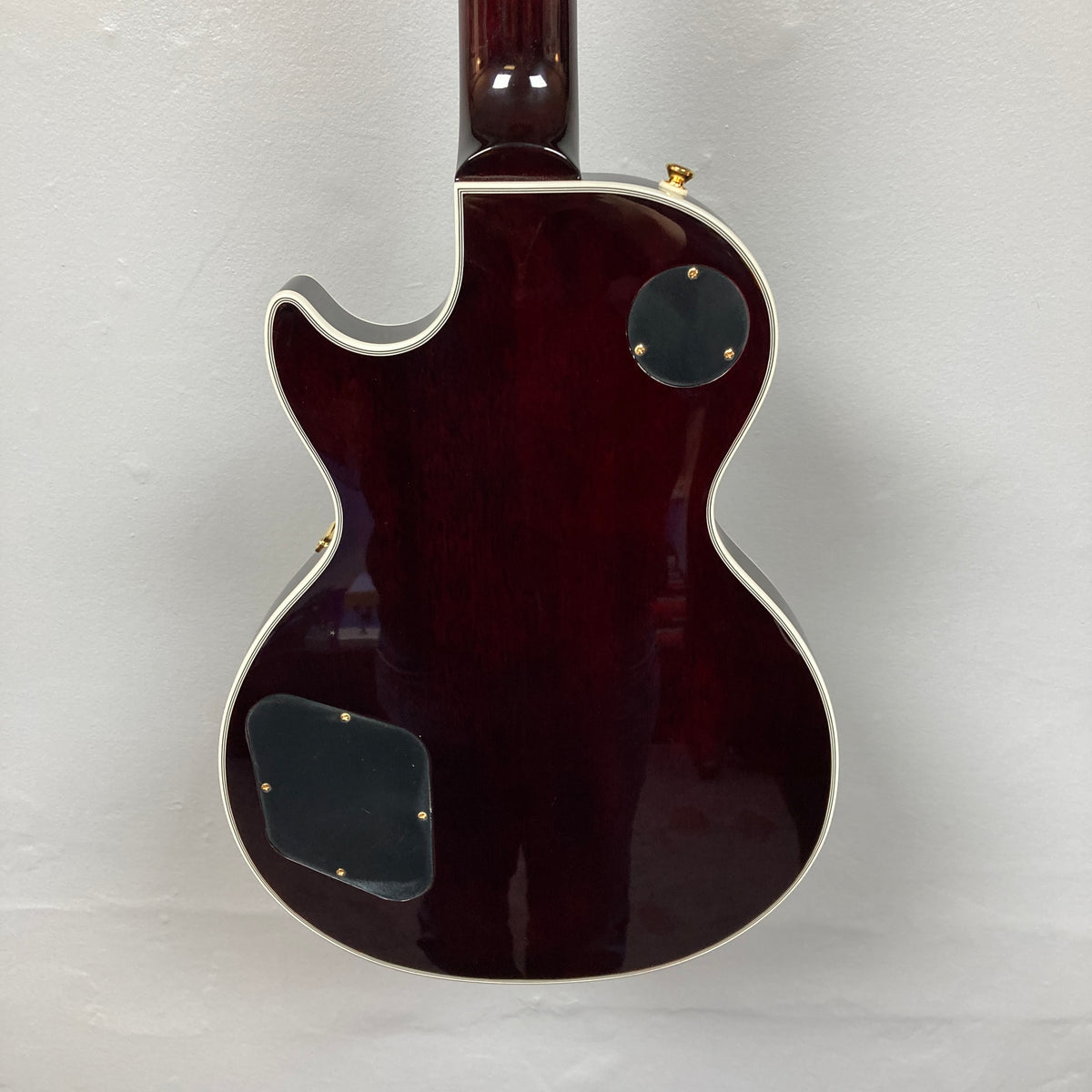Back of the Epiphone Jerry Cantrell Wino Les Paul Custom in Wine Red with cream binding, two access panels, and part of the neck shown against a light background; includes custom Epiphone hardshell case.