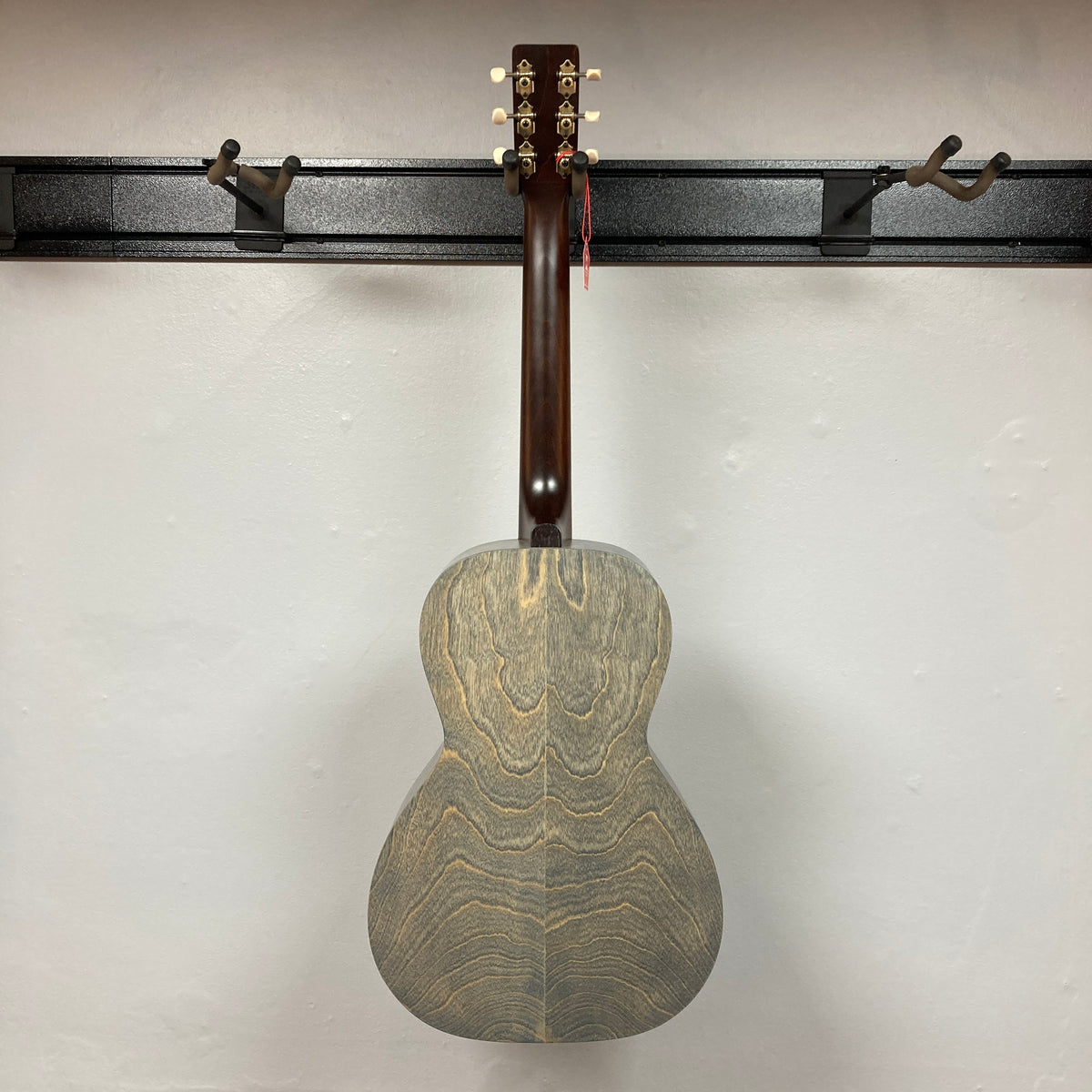 An Art & Lutherie Roadhouse Denim Blue Q-Discrete acoustic guitar hangs by its neck on a black wall-mounted rack against a white wall.