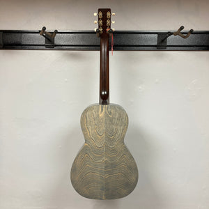 An Art & Lutherie Roadhouse Denim Blue Q-Discrete acoustic guitar hangs by its neck on a black wall-mounted rack against a white wall.