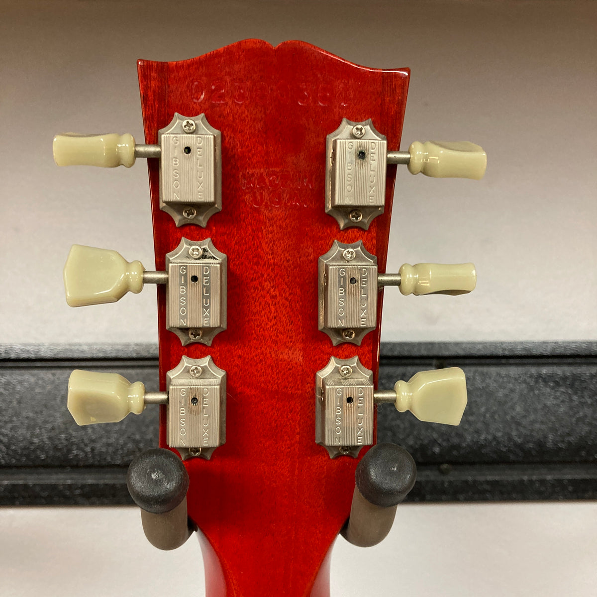 Close-up of the back of a Gibson SG Standard Heritage Cherry yr 2000 Consign headstock by Gibson, featuring six vintage-style tuners and two black wall mount holders—showcasing USA-made quality in every detail.
