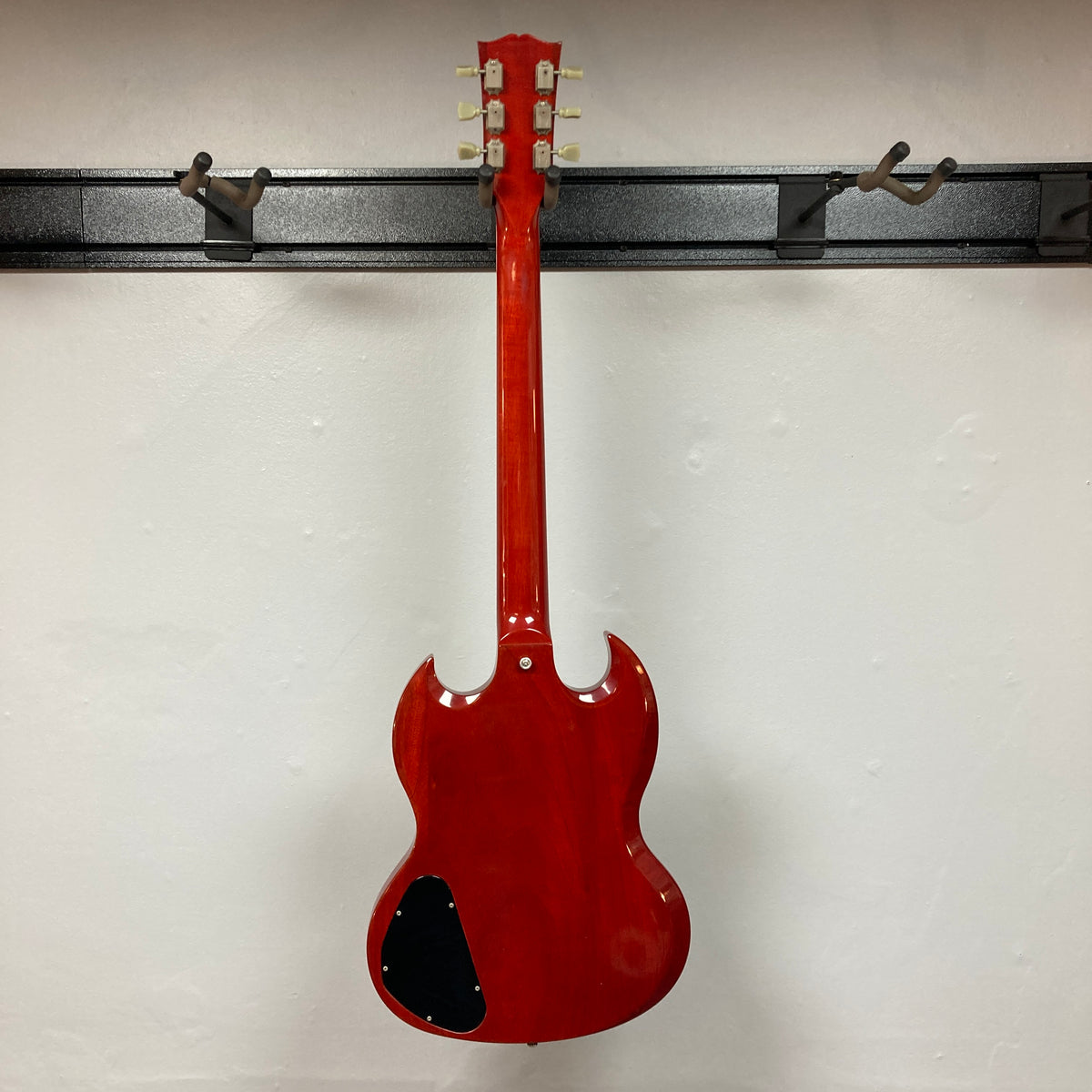 A Gibson SG Standard Heritage Cherry yr 2000 Consign electric guitar, made by Gibson, hangs on a wall rack with its back showing a black plastic cover near the bottom.