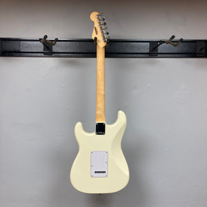 A Fender Standard Stratocaster Olympic White Refurb by Fender hangs on a wall-mounted rack, shown from the back with its neck and tuning pegs clearly visible.