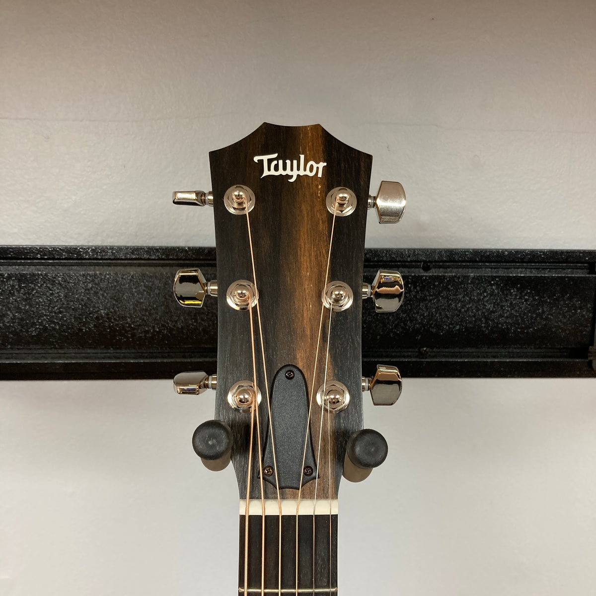 Close-up of a Taylor 212ce Plus w/Gigbag Used Consign headstock, showing six tuning pegs and strings against a plain background.
