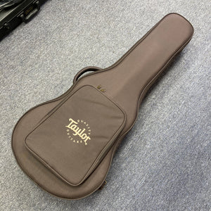 A Taylor 212ce Plus acoustic guitar gig bag with a front pocket, in brown, is on a gray carpeted floor.