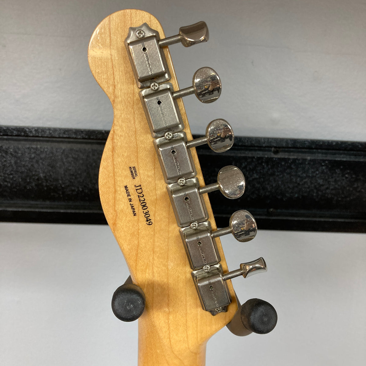 Close-up of the back of a Fender Heritage '60s Telecaster Custom Made in Japan Sunburst headstock, showing six metal tuners and visible serial number, resting on a stand—classic vintage style from Fender.