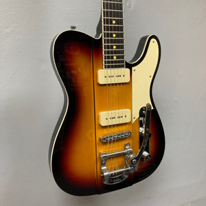 A Reverend Greg Koch Signature Gristle 90 electric guitar in 3-Tone Burst with a white pickguard, two cream-colored Fishman Gristle 90 pickups, Bigsby tremolo, and chrome hardware is shown against a plain gray wall. Brand: Reverend.