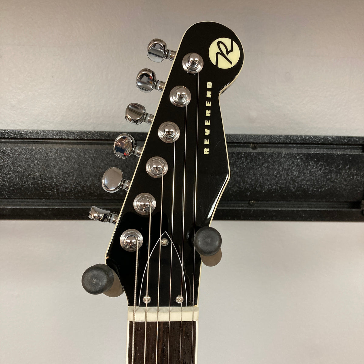 Close-up of the Reverend Greg Koch Signature Gristle 90 3-Tone Burst headstock with six tuning pegs, strings, and Reverend logo on black background; includes gigbag.