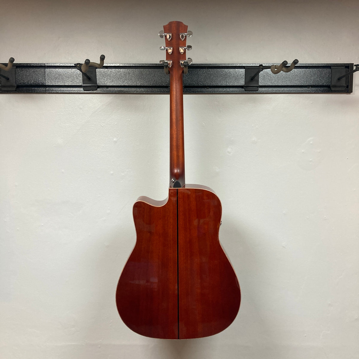 A Yamaha A3M ARE Vintage Natural Acoustic Guitar w/Hard Bag by Yamaha hangs on a black wall-mounted rack, displaying the back of its body and neck against a plain white wall.