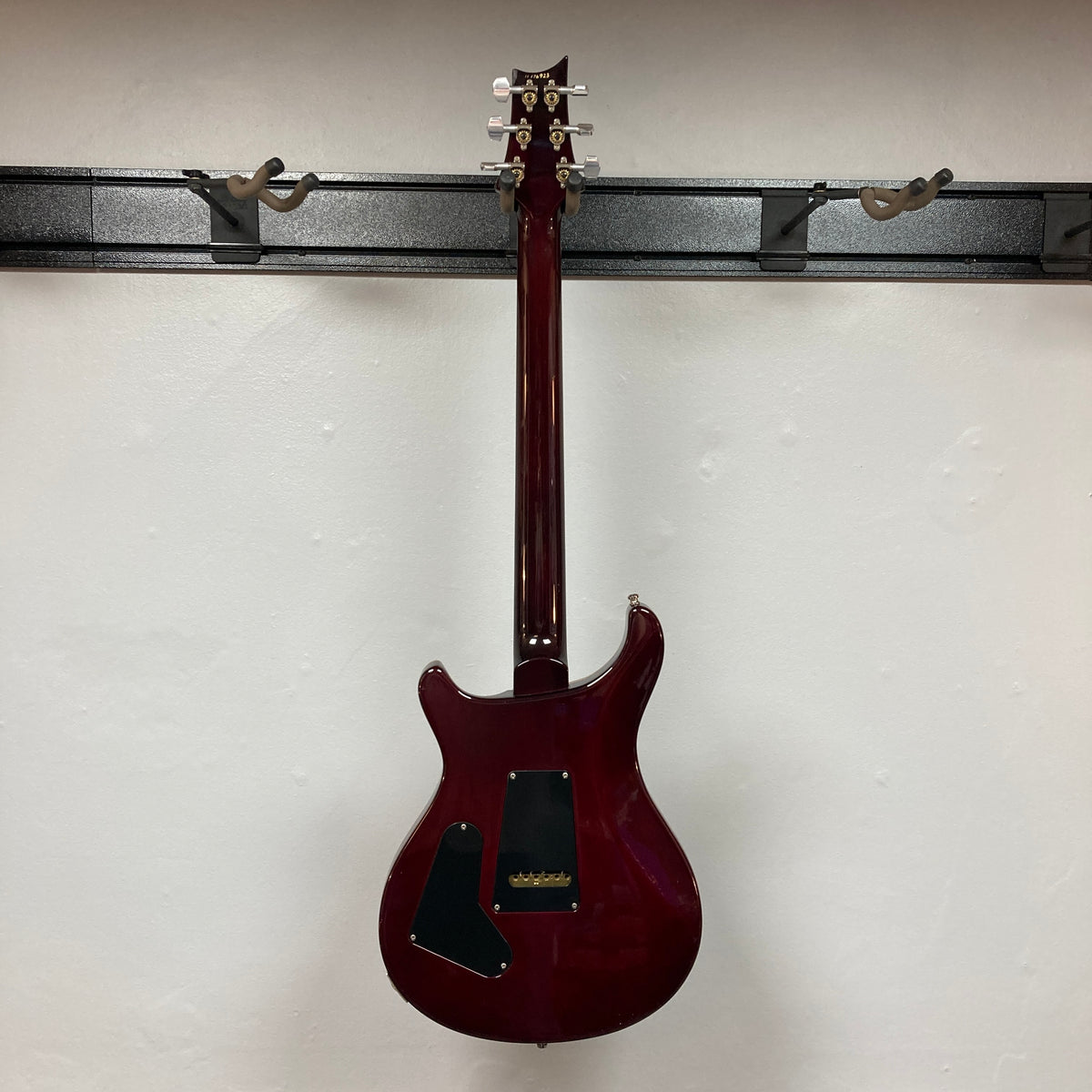 A PRS Custom 24 Violet 2011 electric guitar is shown hanging on a wall mount, photographed from the back against a plain white wall.