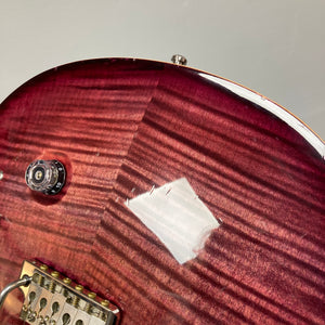 Close-up of a PRS Custom 24 Violet 2011 electric guitar body, showcasing the wood grain, control knob, bridge, and a noticeable area of chipped or worn finish near the top edge. The image highlights PRS’s attention to detail and features such as the 59/09 humbuckers.