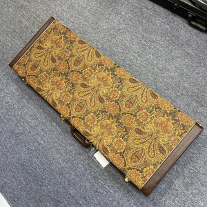 A rectangular case with a brown and gold paisley pattern rests on a gray carpeted floor. Designed to protect your PRS Custom 24 Violet 2011 electric guitar, it features brown leather accents and a sturdy handle—ideal for carrying your prized PRS instrument in style.