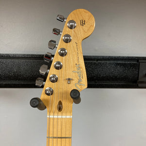 Close-up of a Fender American Standard Strat upgraded Gilmour EMG DC-20 guitar headstock in striking Bordeaux Metallic, featuring six tuning pegs and mounted on a black wall hanger against a light-colored wall. Outfitted with EMG DC-20 David Gilmour pickups, this Fender instrument blends classic style with modern versatility.