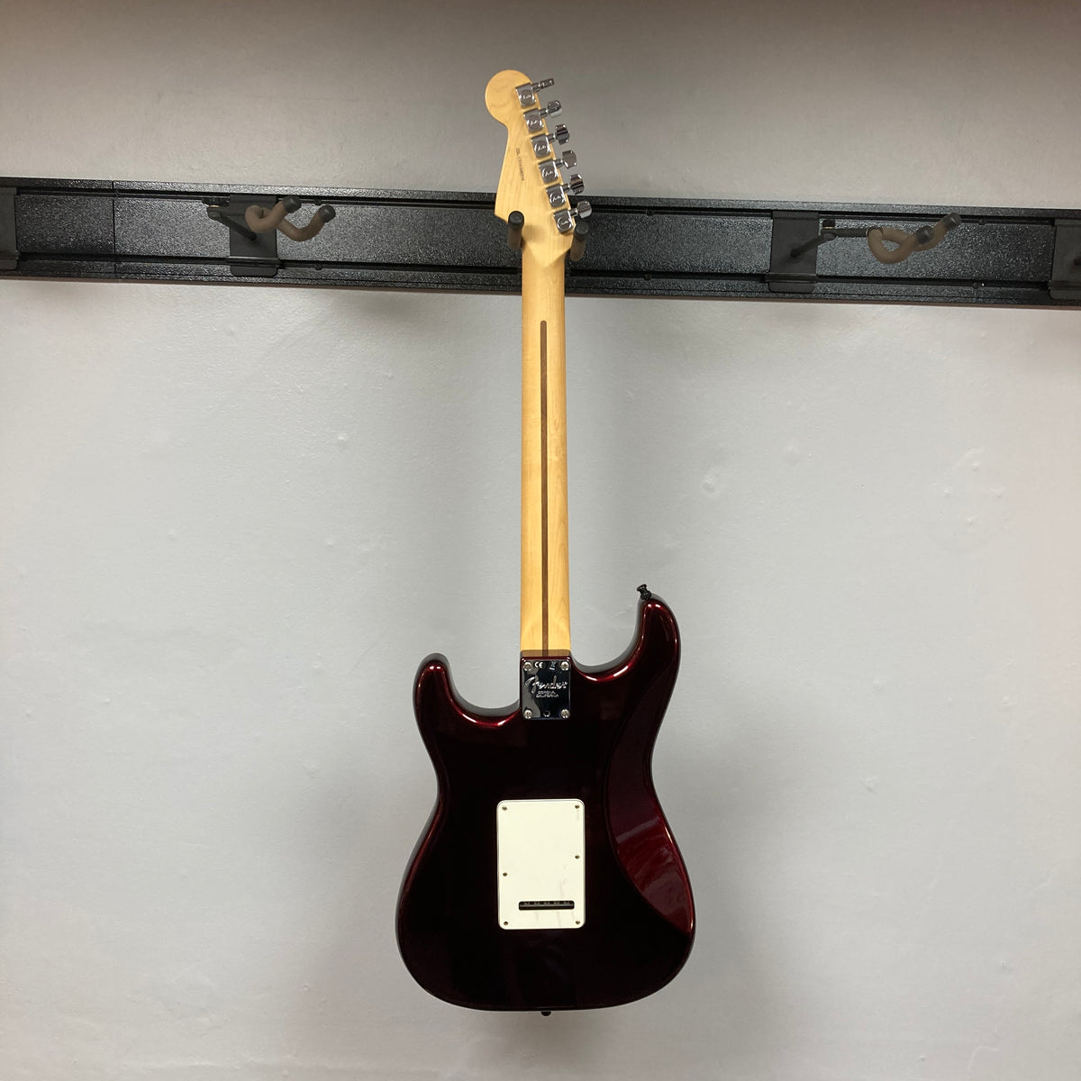 A Fender American Standard Strat upgraded Gilmour EMG DC-20 electric guitar in striking Bordeaux Metallic is displayed hanging on a wall mount, shown from the back with the headstock at the top and the body at the bottom. This model features EMG pickups for that iconic David Gilmour tone.