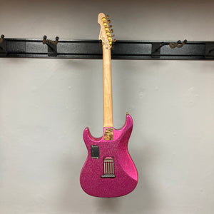 An Edwards ESP E-SN-185-TO Takayoshi Ohmura electric guitar in Twinkle Pink with a glitter finish hangs on a wall-mounted rack, shown from the back to display its neck, tuning pegs, and hardware.