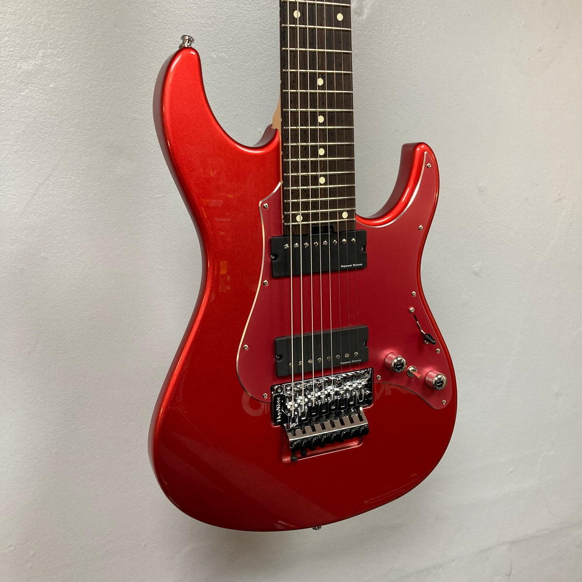 ESP Snapper Raiden 8 ISAO Custom eight-string electric guitar with a glossy red finish, dual humbucker pickups, black pickguard, and a Floyd Rose-style tremolo bridge by ESP—hanging on a white wall and showcasing cutting-edge style; includes gigbag.