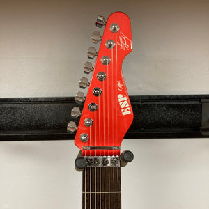 ESP Snapper Raiden 8 ISAO Custom electric guitar headstock by ESP, featuring eight tuning pegs, a signature, and logo, displayed on a wall hanger against a solid Raiden Red background.