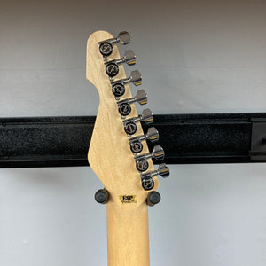Back of a guitar headstock showing six chrome tuning pegs, a maple neck, and an ESP logo against a white wall and black rack—highlighting the exceptional craftsmanship of the ESP Snapper Raiden 8 ISAO Custom w/Gigbag by ESP in vivid Raiden Red.
