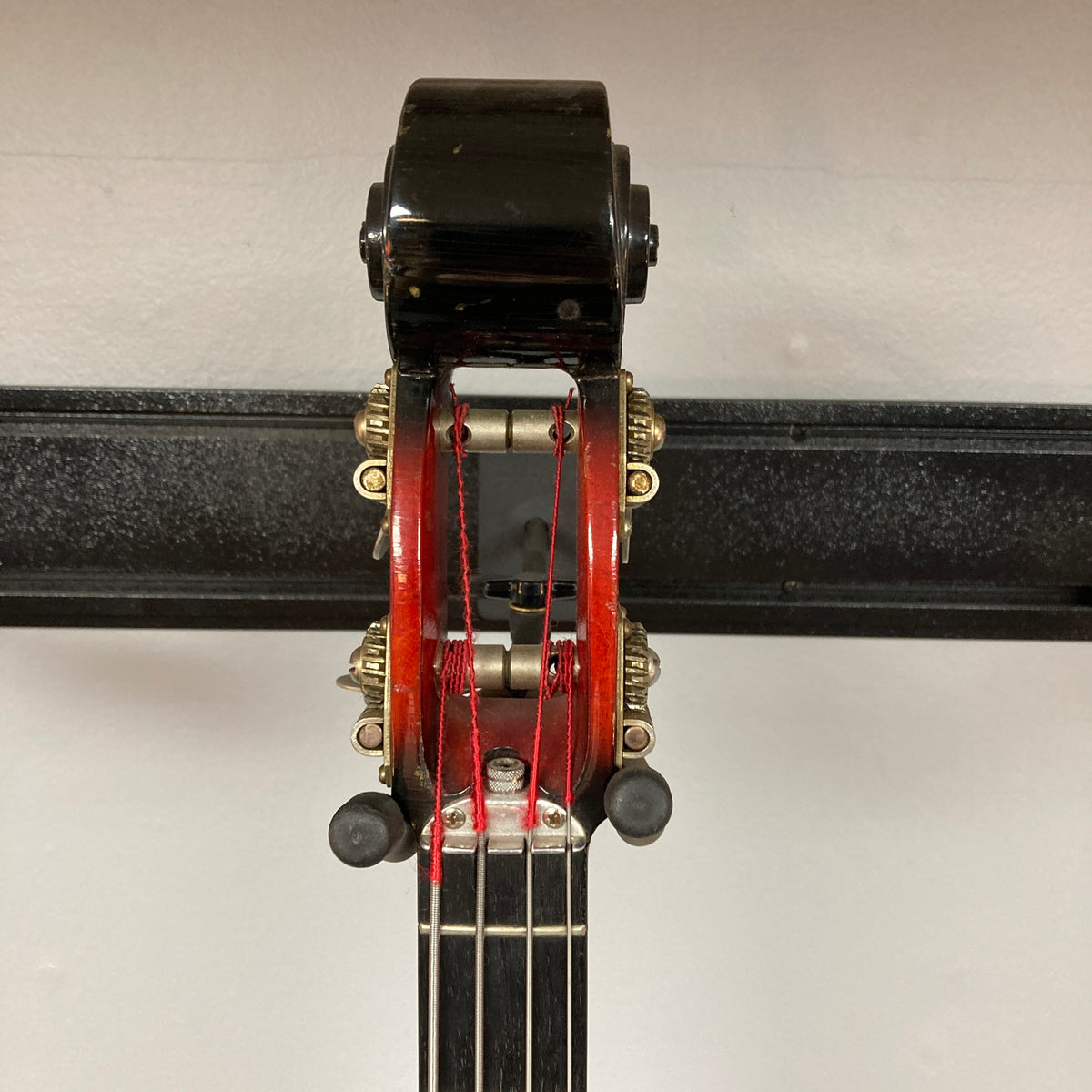 Close-up of the top of a string instrument showing tuning pegs, strings, and a black metal support rack against a white background, echoing the distinctive details seen on vintage Ampeg models such as the 1966 Ampeg ASB-1 Devil Bass Serial #531 w/Case.