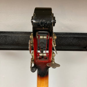 Close-up of the back of a 1966 Ampeg ASB-1 Devil Bass (Serial #531) headstock, highlighting tuning pegs, gears, red string windings, and the wooden neck against a plain wall—capturing the classic details characteristic of this iconic Ampeg instrument.