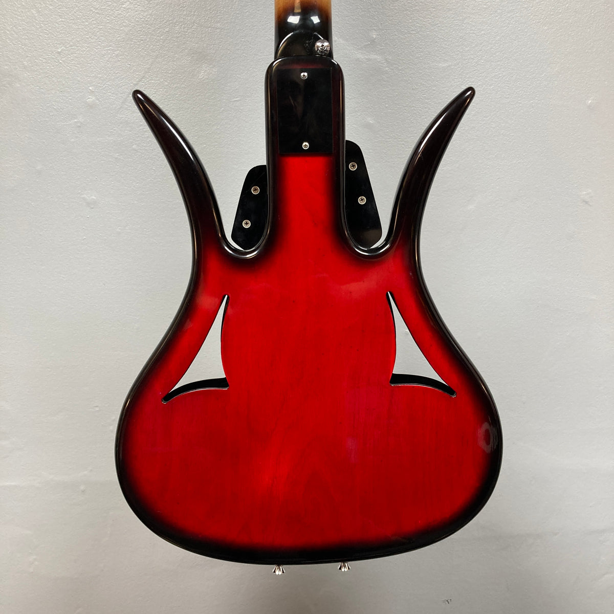 The back of an Ampeg 1966 ASB-1 Devil Bass (Serial #531) with a glossy red finish, distinctive curved horns, and two f-shaped sound holes is shown against a plain light-colored wall.
