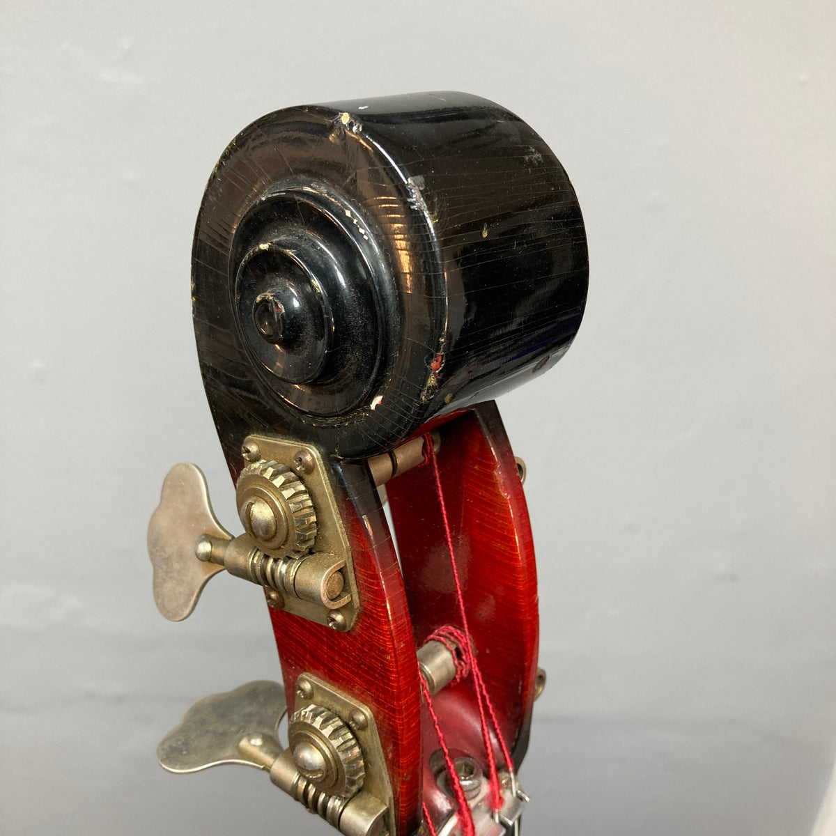 Close-up of the scroll and tuning pegs on an Ampeg 1966 ASB-1 Devil Bass (Serial #531), featuring red varnish and metal hardware reminiscent of a vintage upright, set against a plain gray background.