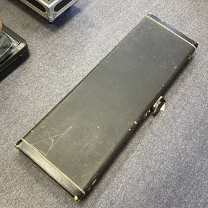 A closed, rectangular black hard case from Ampeg rests on a blue carpeted floor. Showing visible scratches and scuffs, the case suggests a history of use, possibly having once protected an instrument like the 1966 Ampeg ASB-1 Devil Bass (Serial #531) with its unique bridge-mounted transducer pickup.
