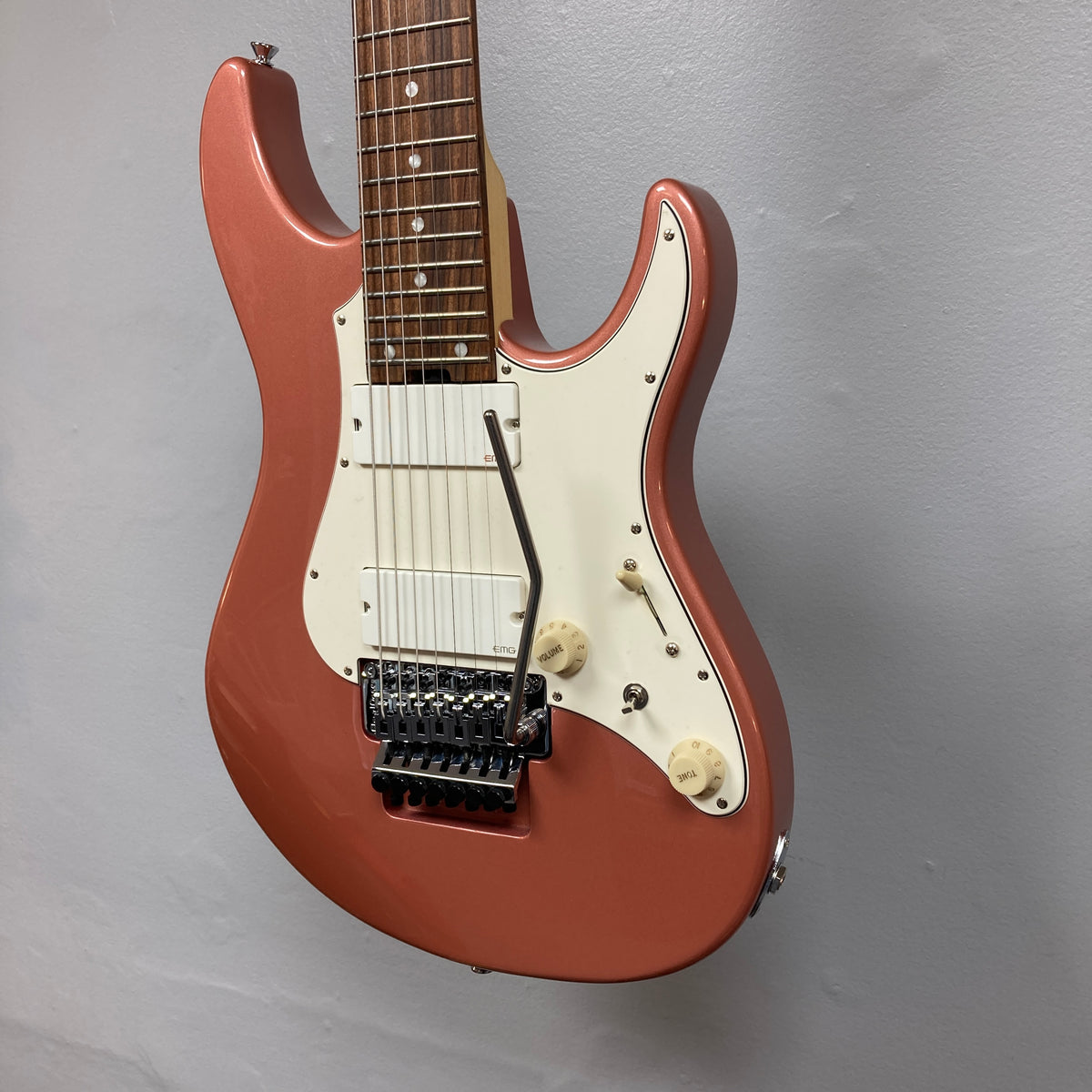 An Edwards E-SN7-194MF Mikio Fujioka Signature Burgundy Mist 7-string electric guitar, featuring a metallic red finish, white pickguard, two control knobs, and a whammy bar, is mounted on a wall with a plain light gray background.