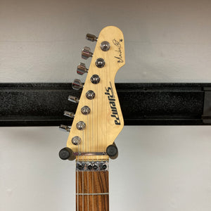 Close-up of the headstock of an Edwards E-SN7-194MF Mikio Fujioka Signature guitar in Burgundy Mist, featuring six tuning pegs, the “Edwards” logo, and Mikio Fujioka’s signature set against a light wood background. The neck displays a striped wood pattern characteristic of this signature model.