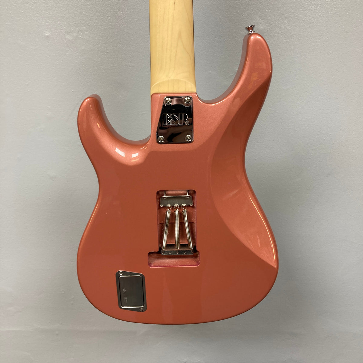 Back of an Edwards E-SN7-194MF Mikio Fujioka Signature seven-string guitar in Burgundy Mist, featuring a visible metal neck plate, spring cavity, and rectangular compartment, shown against a plain light gray wall.