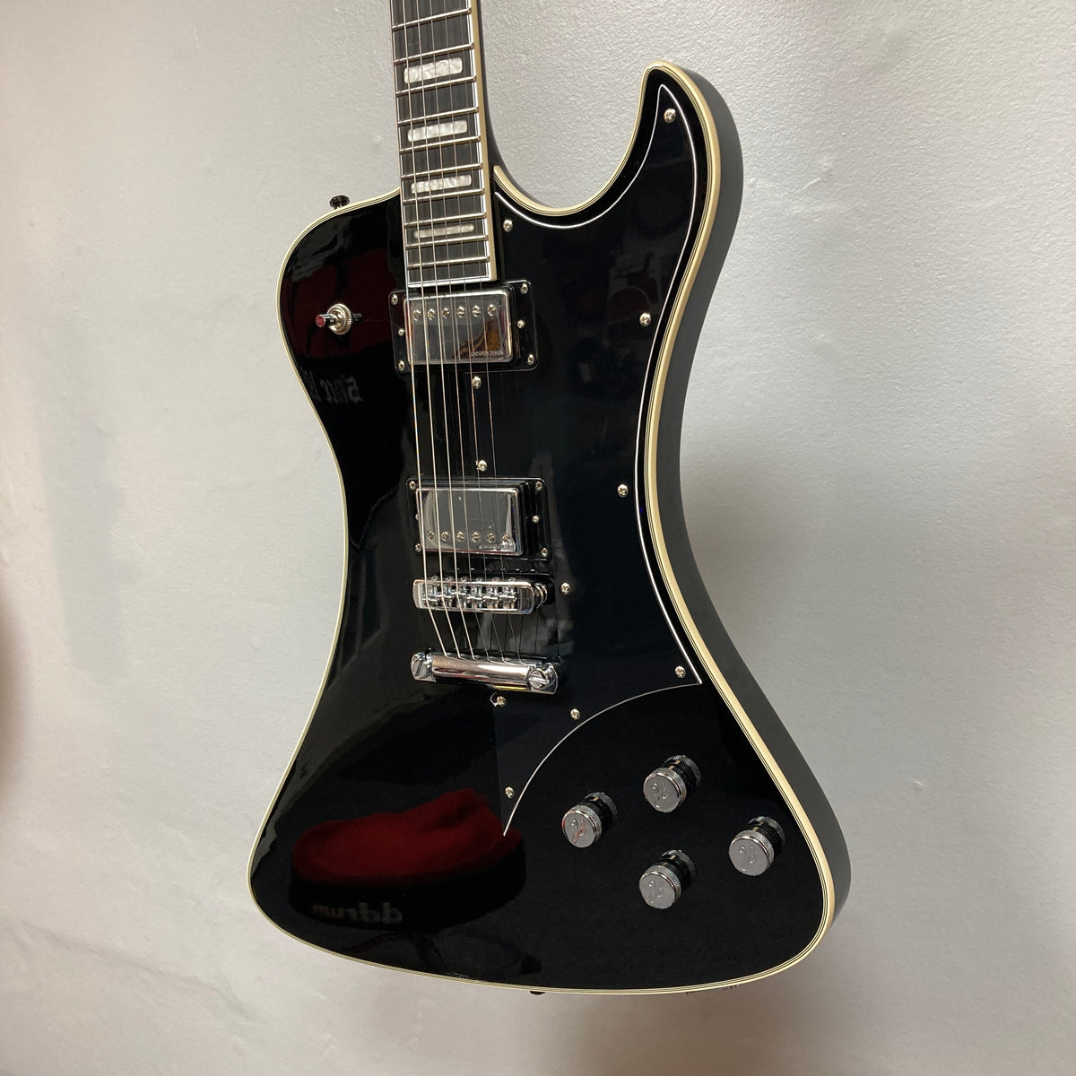 The Hagstrom Fantomen Custom Black w/case electric guitar by Hagstrom features a glossy black finish, cream binding, chrome hardware, a pair of Lundgren Design humbuckers, four control knobs, and a three-way pickup selector switch. It is displayed hanging against a white wall.