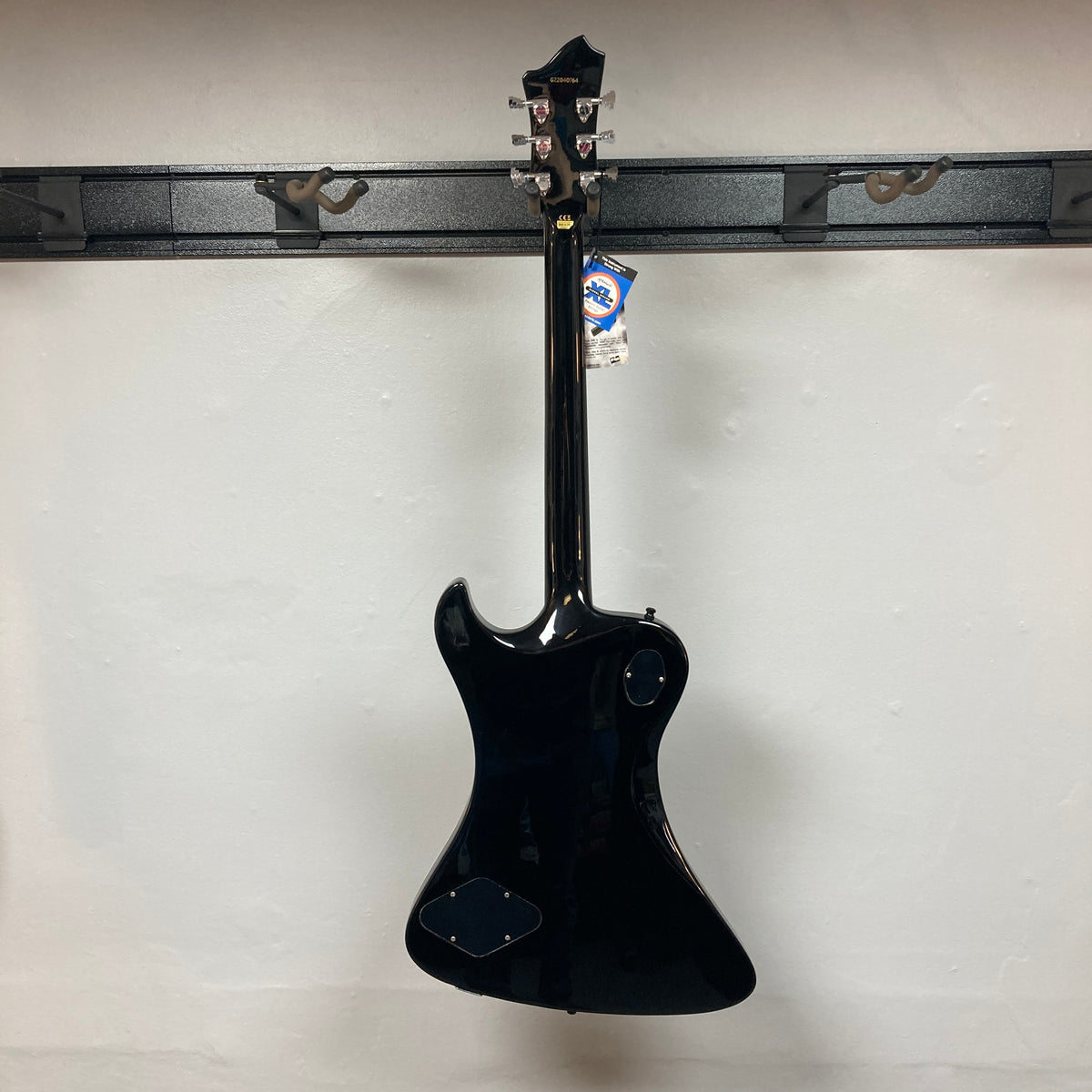 A Hagstrom Fantomen Custom Black w/case electric guitar by Hagstrom hangs on a wall rack, displayed from the back with a tag attached to the headstock.