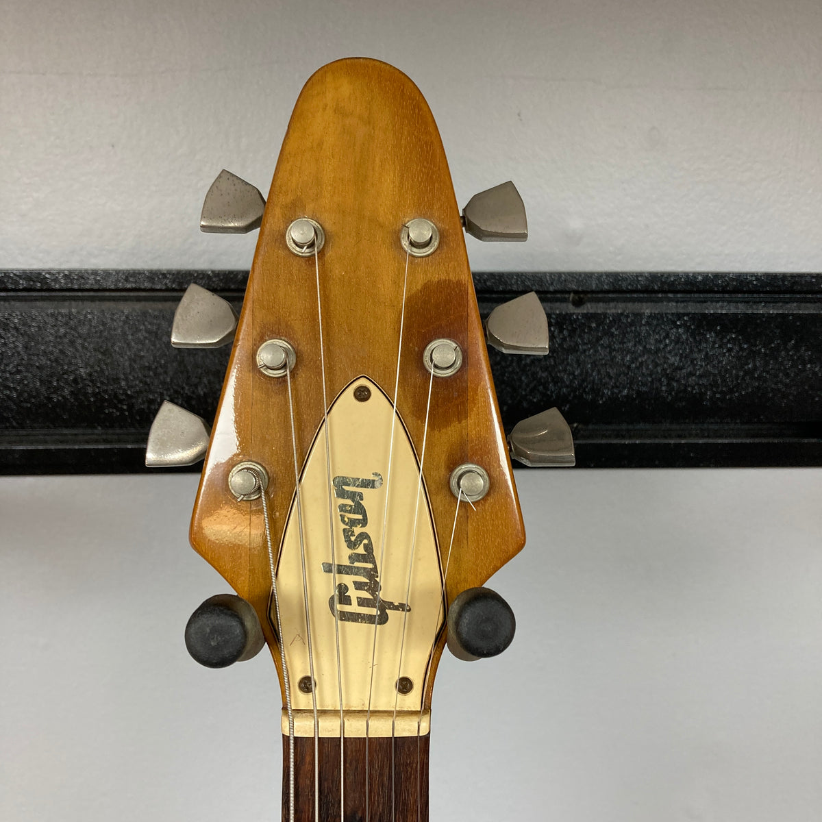 A close-up of the headstock of a 1975 Gibson Flying V w/Case by Gibson, featuring six tuning pegs, a natural finish, and the brand’s logo displayed on a metal plate.