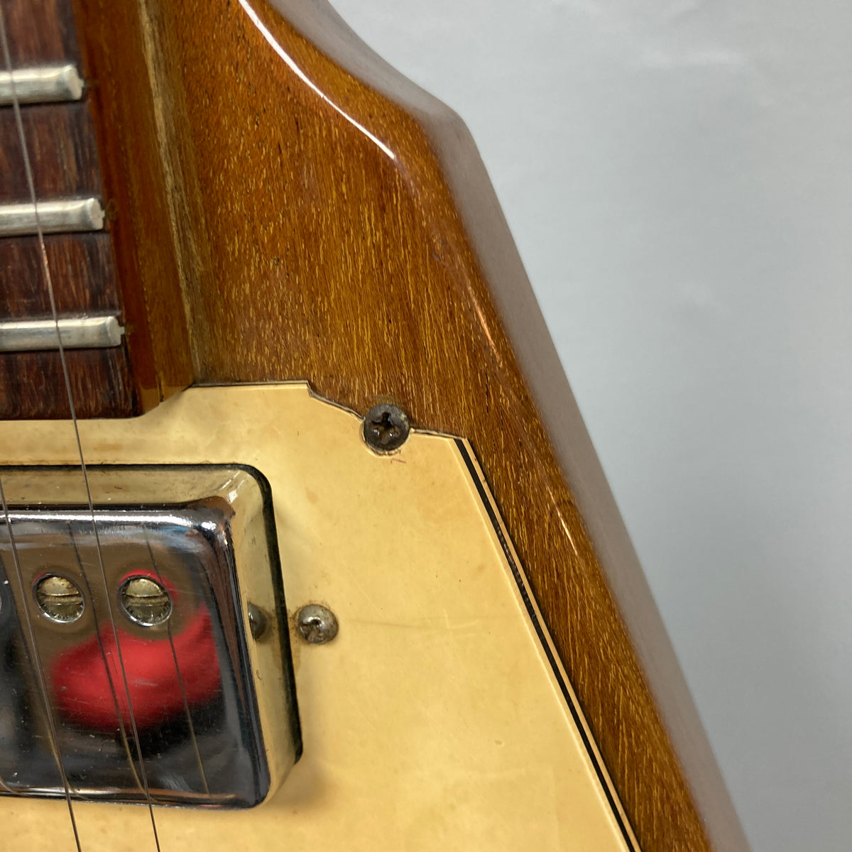 Close-up of a 1975 Gibson Flying V electric guitar with a natural finish, featuring part of the fretboard, a chrome pickup, cream-colored pickguard, and a screw on the wooden body—showcasing classic Gibson craftsmanship.