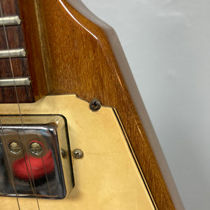 Close-up of a 1975 Gibson Flying V electric guitar with a natural finish, featuring part of the fretboard, a chrome pickup, cream-colored pickguard, and a screw on the wooden body—showcasing classic Gibson craftsmanship.