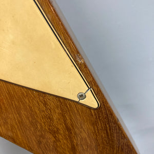 Close-up of the 1975 Gibson Flying V w/Case by Gibson, featuring a wooden body with a triangular yellow plate fastened by a single screw, displaying surface scratches and wear that highlight its natural vintage finish.