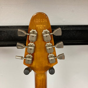 Close-up of the back of a Gibson 1975 Flying V w/Case headstock, displaying six tuning pegs, serial number 400136, and “Made in U.S.A.” engraved on the natural finish wood.