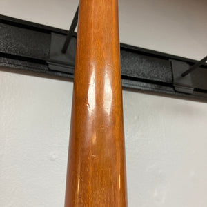 Close-up of the neck of a 1975 Gibson Flying V w/Case by Gibson, featuring a natural wood finish with visible indentations and minor scratches. Displayed against a white wall and black metal wall hanger, the wear enhances the vintage character distinctive to this classic instrument.