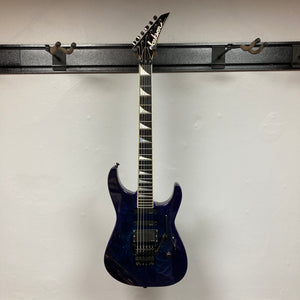 A 1995 Jackson SL1 Soloist Custom Shop Eerie Dess Swirl electric guitar by Jackson, featuring a pointed headstock and triangular inlays, is displayed on a wall-mounted guitar rack against a plain white wall.